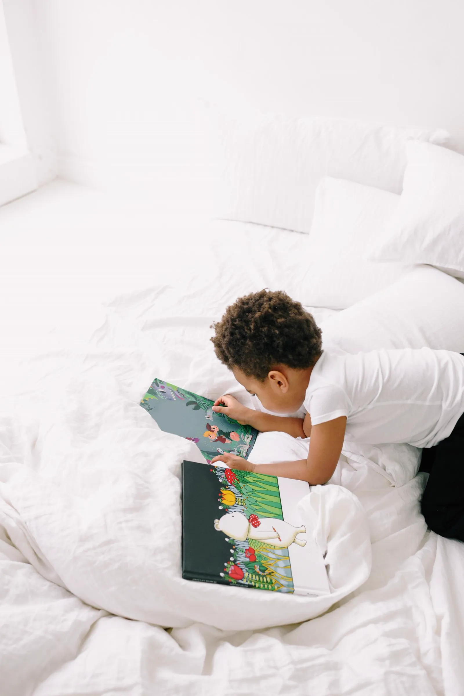 A boy reads picture books sprawled across a bed