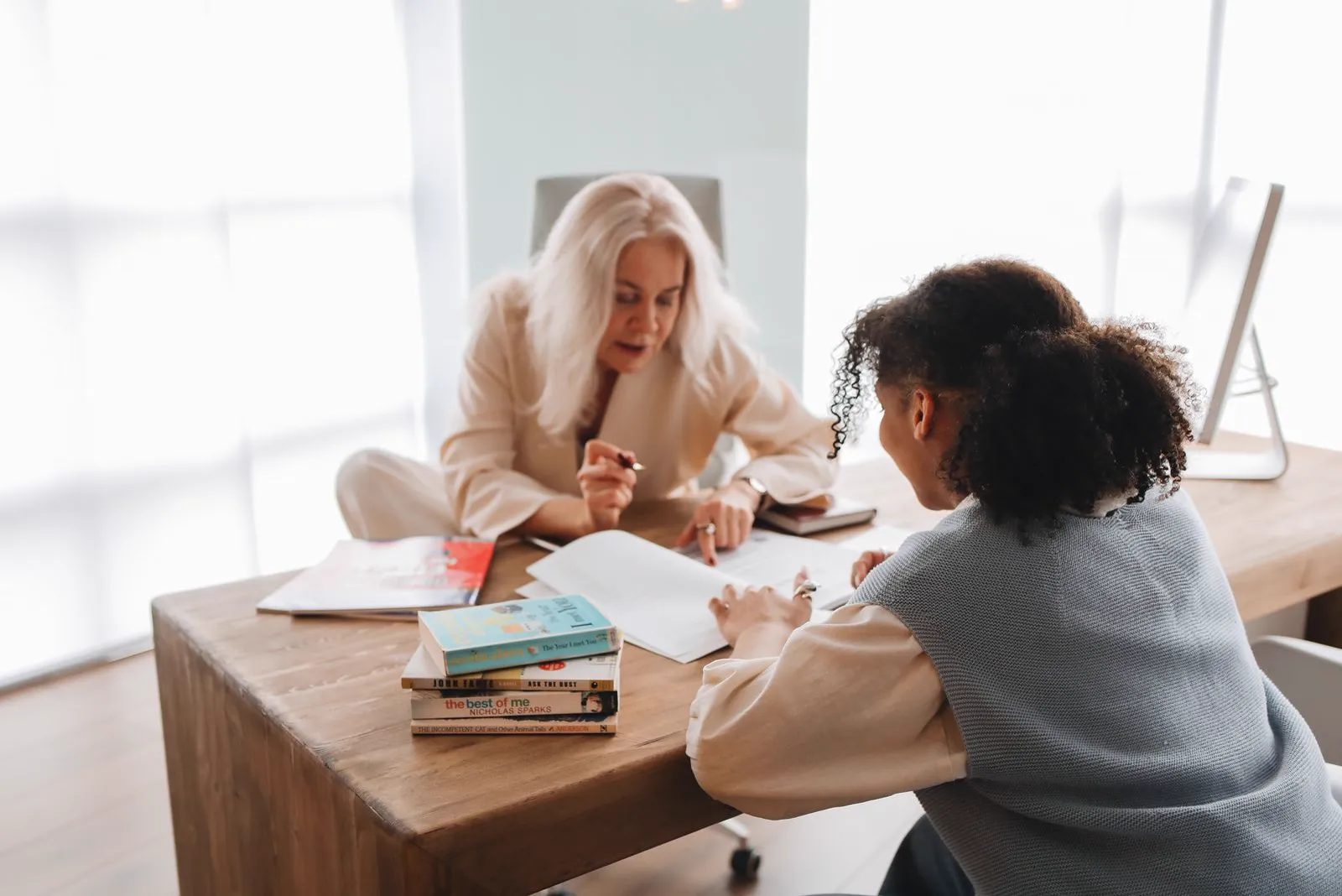 A teacher and student compare work across a desk